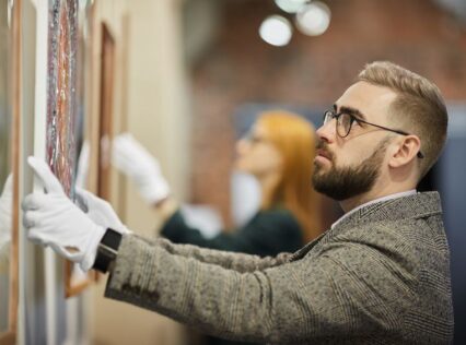 Bearded man with gloves appraising a piece of art