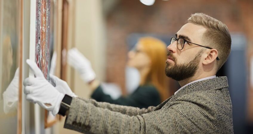 Bearded man with gloves appraising a piece of art